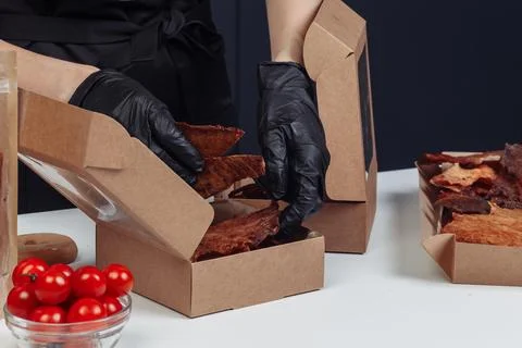 A guy puts dried meat in paper boxes in black gloves Stock Photos