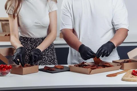 A guy puts dried meat in paper boxes in black gloves Stock Photos