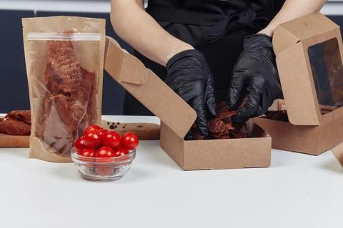 A guy puts dried meat in paper boxes in black gloves Stock Photos