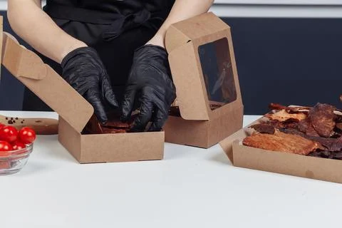A guy puts dried meat in paper boxes in black gloves Stock Photos