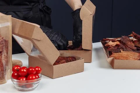 A guy puts dried meat in paper boxes in black gloves Stock Photos