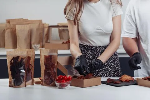 A guy puts dried meat in paper boxes in black gloves Stock Photos