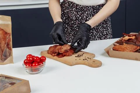 A guy puts dried meat in paper boxes in black gloves Stock Photos