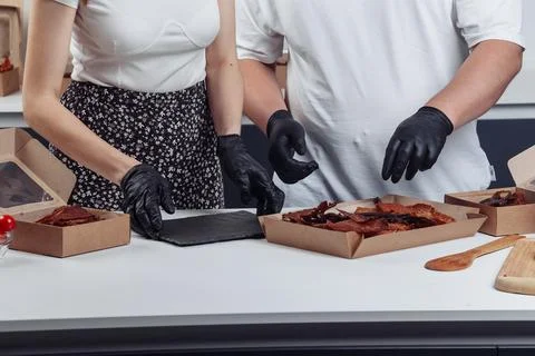 A guy puts dried meat in paper boxes in black gloves Stock Photos