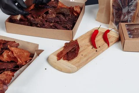 A guy puts dried meat in paper boxes in black gloves Stock Photos