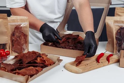 A guy puts dried meat in paper boxes in black gloves Stock Photos