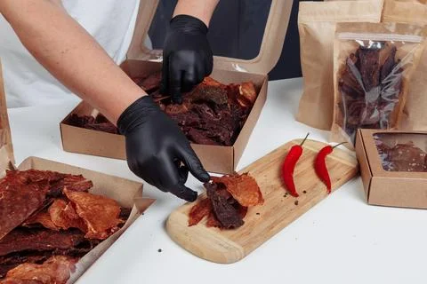 A guy puts dried meat in paper boxes in black gloves Stock Photos