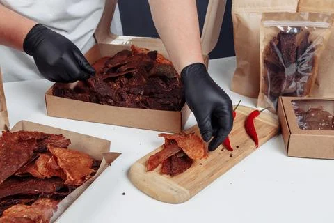 A guy puts dried meat in paper boxes in black gloves Stock Photos
