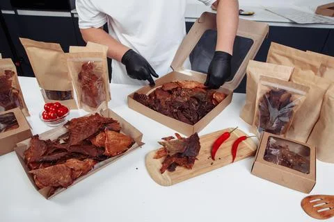 A guy puts dried meat in paper boxes in black gloves Stock Photos