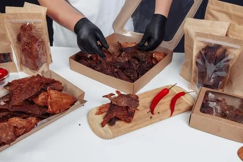A guy puts dried meat in paper boxes in black gloves Stock Photos