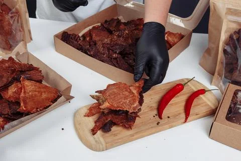 A guy puts dried meat in paper boxes in black gloves Stock Photos