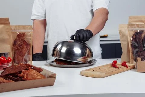 A guy puts dried meat in paper boxes in black gloves Stock Photos