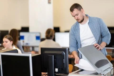 Guy puts paper document into copier, makes copy using office appliances Stock Photos