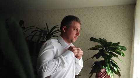 The guy puts on a white shirt while standing in front of a light window. Stock Footage 138115204