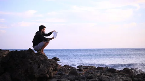 Guy reading a book crouched on the rock Stock Footage 58117235