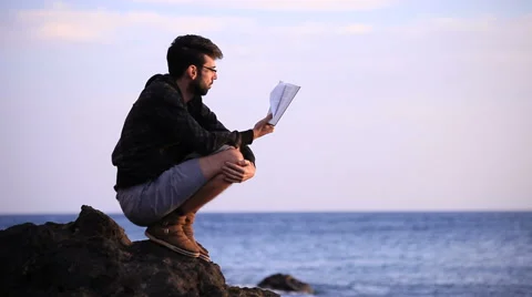 Guy reading a book crouched on the rock Stock Footage 58117584