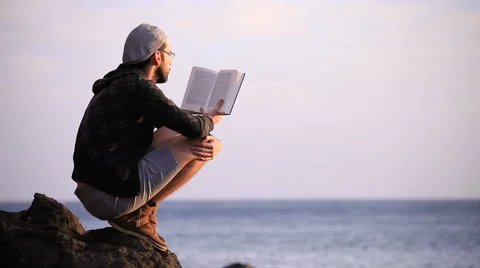 Guy reading a book on a rock Video stock 58120793