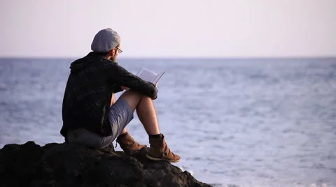 Guy reading a book on a rock Video stock 58122928