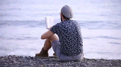 A guy reading a book sitting on the beach Stock-Footage 58215577
