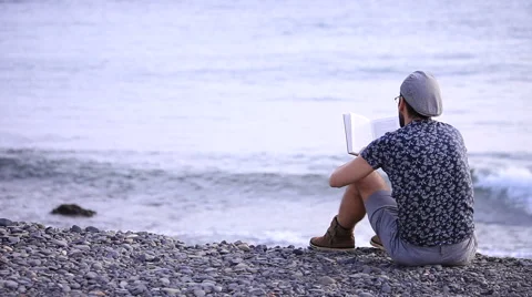 A guy reading a book sitting on the beach Stock Footage 58216950