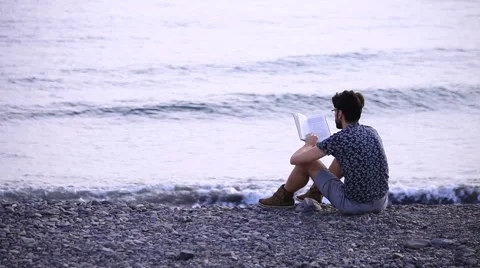 A guy reading a book sitting on beach Stock Footage 58228771