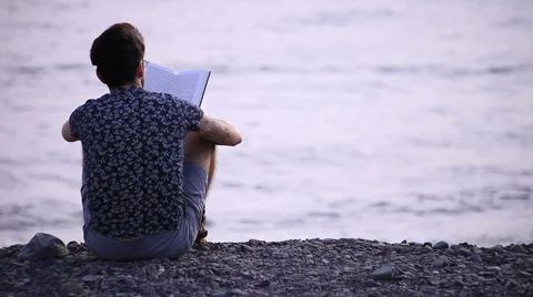 A guy reading a book sitting on beach Video stock 58233992