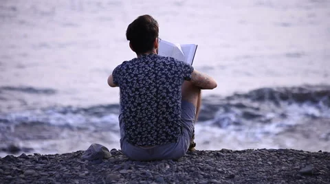 A guy reading a book sitting on beach Stock-Footage 58235315