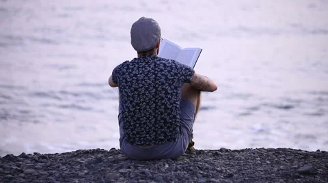 A guy reading a book sitting on beach Stock Footage 58236997