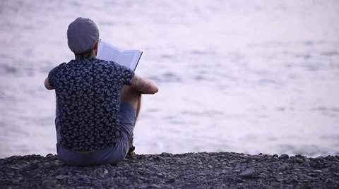 A guy reading a book sitting on beach Stock Footage 58237923