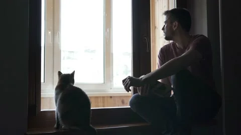 The guy reads a book sitting on the windowsill in the house Stock Footage 128438313