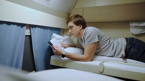 A guy reads a book while lying in a train compartment. Stock Footage 105259711