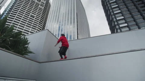 A Guy in red and black clothes jumping and practicing parkour Stock Footage 264199813