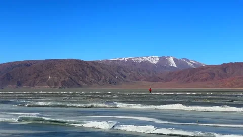 Guy in a red jacket walks on a frozen lake in the mountains. Long shot Stock-Footage 232653223