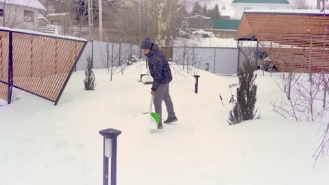 The guy removes snow from the path in his area between young trees. Stock Footage 154907019