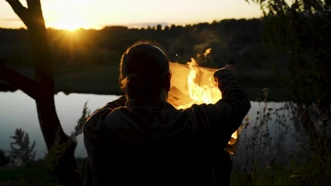 The guy is resting against the sunset with a burning newspaper in his hands Stock Footage 138143020