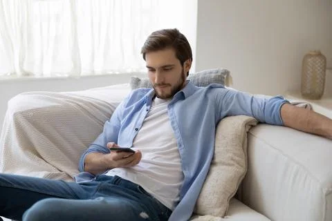 Guy resting on sofa using smartphone read social media news Stock Photos