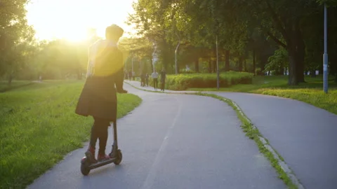 A guy rides along the path on an electric scooter with his back to the camera. 库存影片 201073907