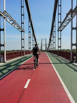 A guy rides a bicycle with a backpack on a path on a bridge in perspective Stock Photos