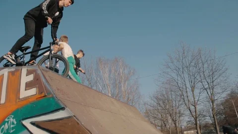 Guy rides a bicycle on a ramp A group of teenagers ride scooters and skateboards Stock-Footage 108691305