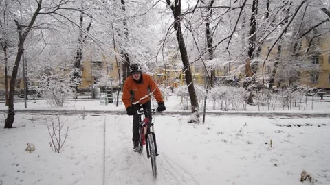 A guy rides a bicycle through a winter city among snow-covered trees Stock Footage 260460227
