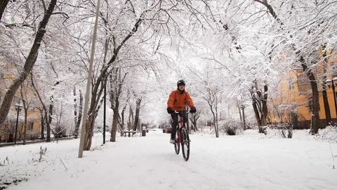 A guy rides a bicycle through a winter city among snow covered trees Stock Footage 260460342
