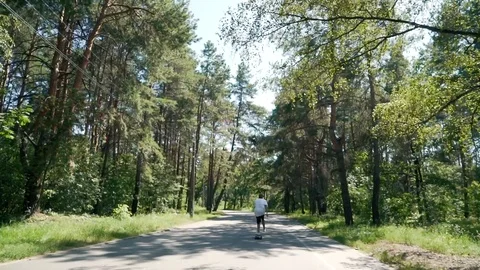 A guy rides a skateboard on an empty road in park Stock Footage 99678460