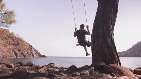 The guy rides on a swing in a beautiful bay Stock Footage 211689655