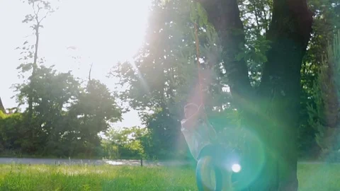 The guy rides a swing from the tire, beautifully painted in the garden at sunset Stock Footage