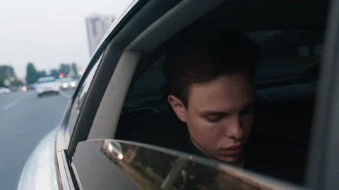 A guy rides in a taxi with an open window, looks at the phone, out the window. 動画素材 208647850