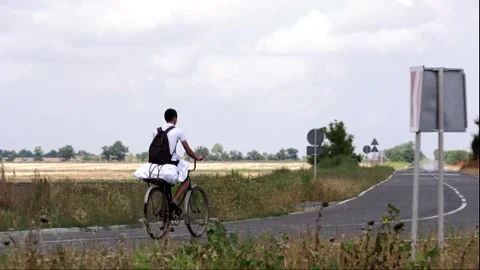 A guy is riding a bicycle along a long road between fields Stock Footage 324766759