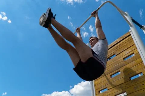 The guy is rocking the press on the horizontal bar. Workout outdoors. Blue sk Stock Photos