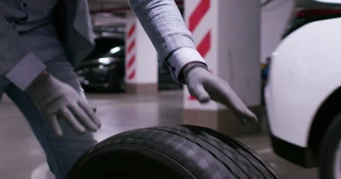 Guy rolls wheel tire in front of car in underground garage Stock Footage 294609735