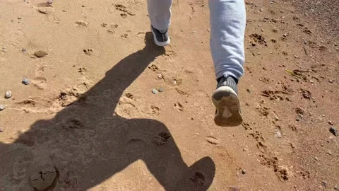 A guy is running along the beach in gray pants and gray sneakers Stock Footage 130435828