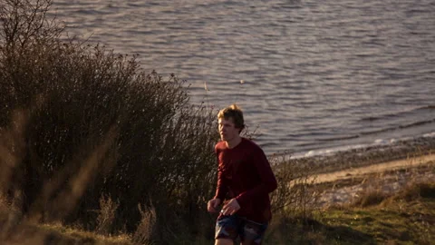 Guy running infront of ocean backlight flare Stock Footage 153516327